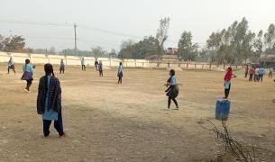 Girls in school uniforms play cricket on an outdoor field