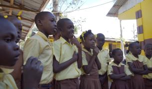 Haitian students in their yellow and brown school uniforms gather in a school courtyard