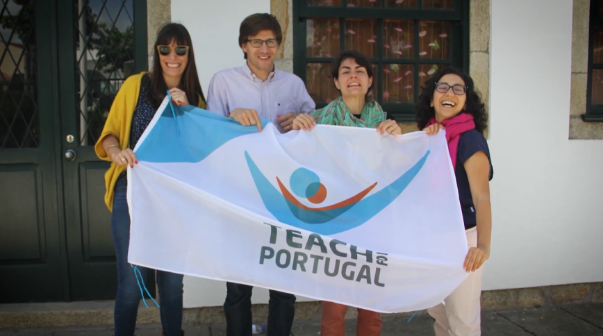 A man and three women, all white with brown hair, smile while holding a flag that says Teach For Portugal