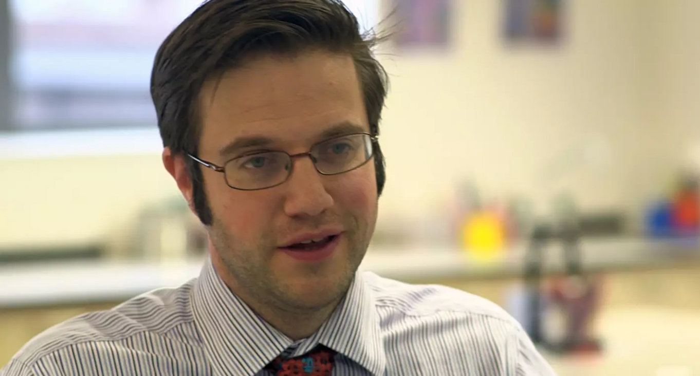 Preview image for the video "Alumni Changemakers: Ed Vainker" - Close up headshot of a young white man with brown hair and glasses wearing a shirt and tie.