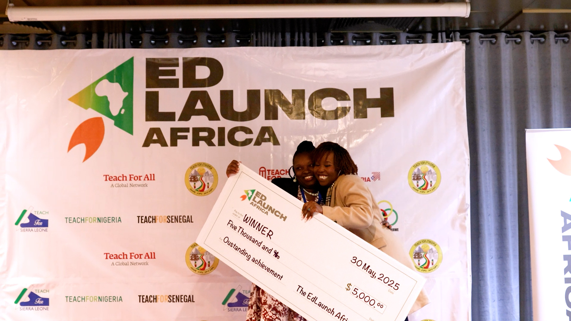 Preview image for the video "EdLaunch Africa 2025". Preview image for the video "EdLaunch Africa 2025" - Two Black women hug while holding a giant check in front of a backdrop that says EdLaunch Africa.