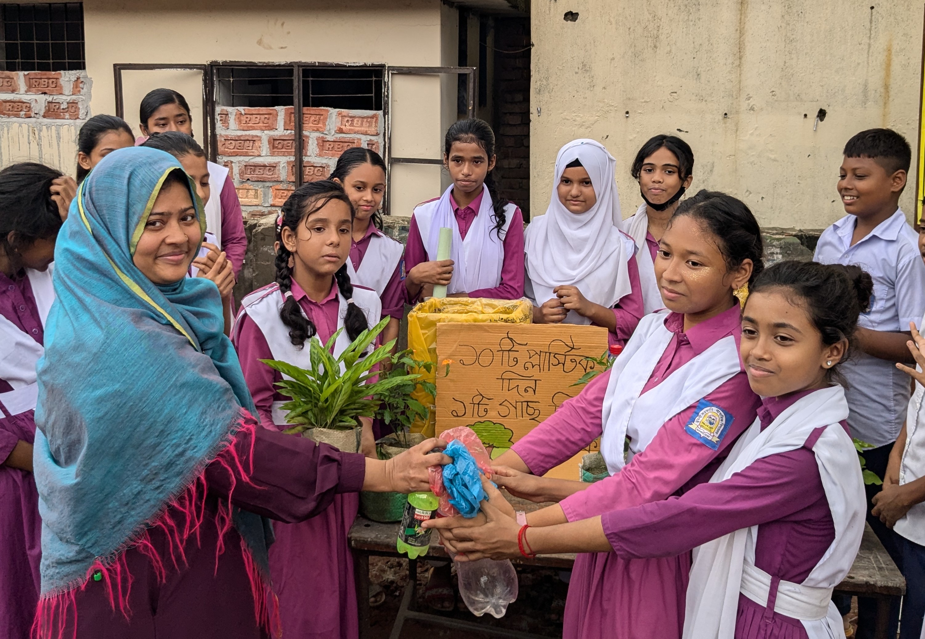 A group of South Asian girls in purple school uniforms with white sashes surrounds a project