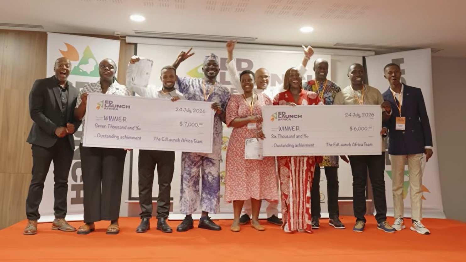 A group of nine Black men and women, some in cultural attire, pose and celebrate on stage as winners of EdLaunch Africa, holding two oversized presentation checks dated July 24, 2026.