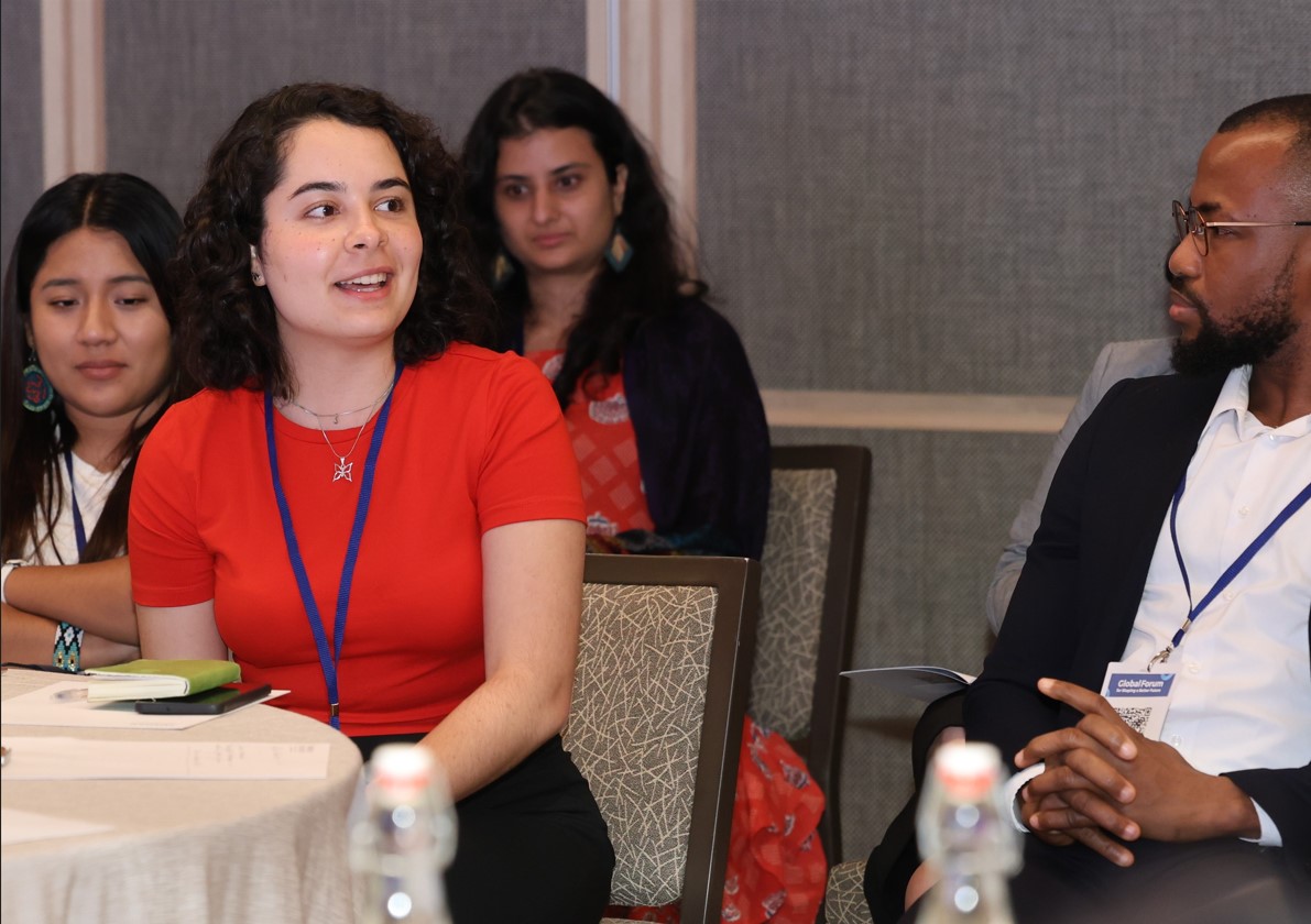 A young woman with shoulder-length curly black hair in a red shirt faces a young Black man with glasses