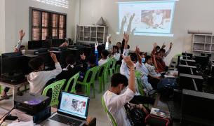 Students raise their hands while viewing a presentation in a computer lab