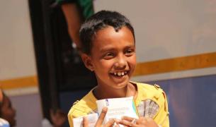 Close up of a young South Asian child holding relief supplies and smiling