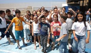 A large group of young Lebanese children pose for a photo in an outdoor courtyard smiling and laughing