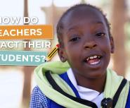 A young african student speaks into a handheld microphone, she is wearing a red shirt that says "Teach For All student leader"