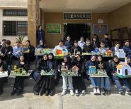 Many children in school uniform sit on steps outside their schools holding models of homes