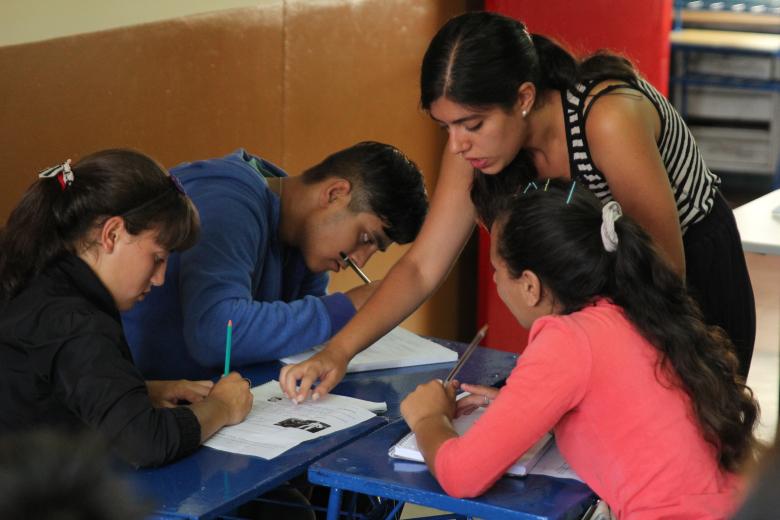 An Ensena Uruguay teacher helps three high school students with worksheets