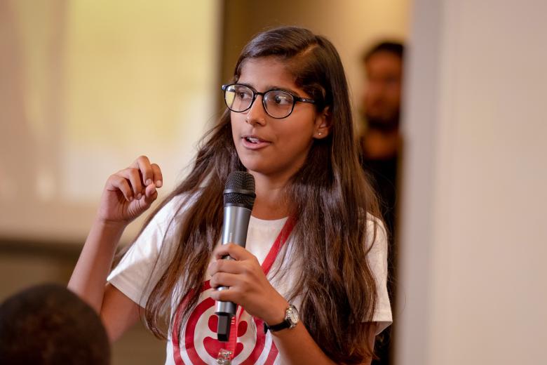 A teenage South Asian girl holds a microphone while speaking