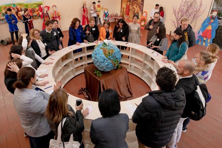 A diverse group of adults stands in a circle surrounding a hand-made globe