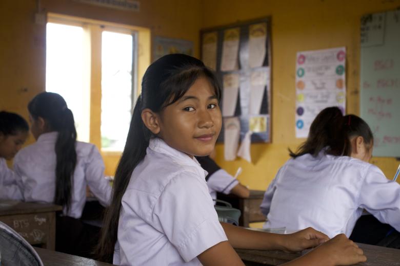 An Asian girl with bangs and a ponytail in a white shirt smiles slightly at the camera