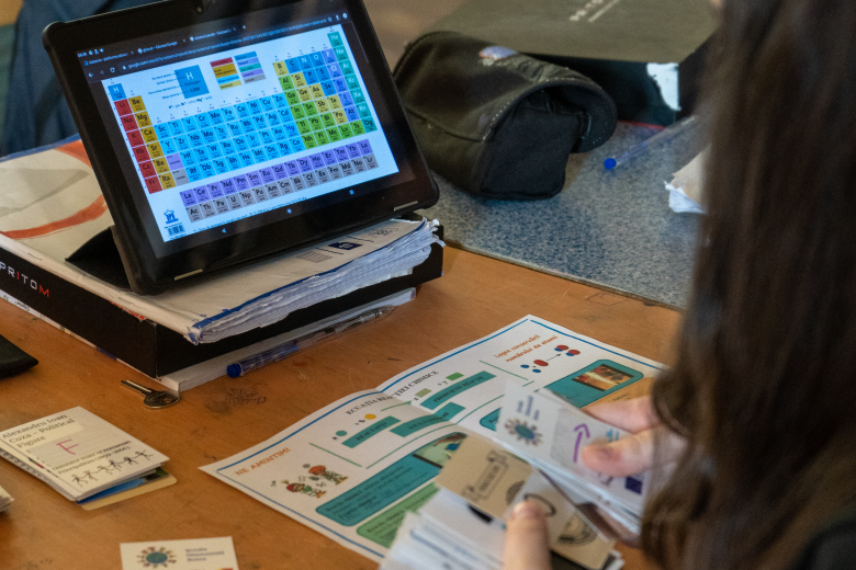 A girl sorts cards as she looks at a small computer screen with colored blocks on it 