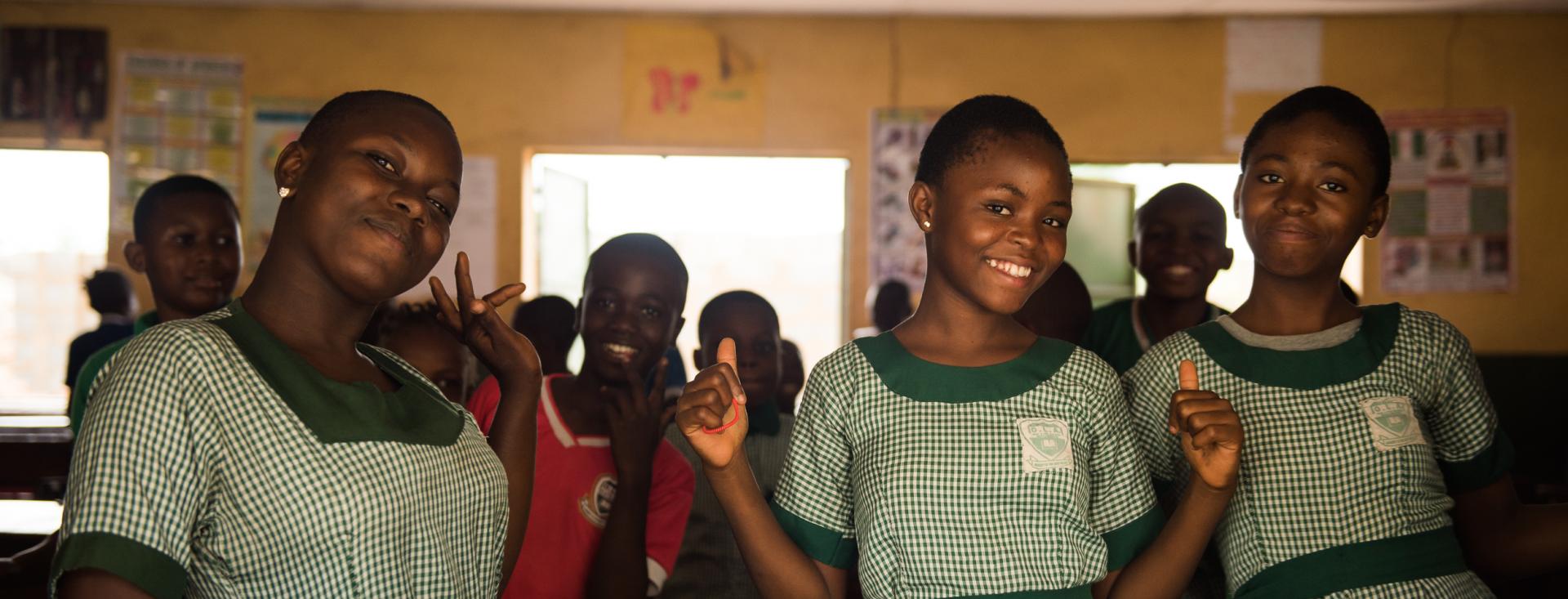 Three Black girls in green checked school uniforms smile at the camera