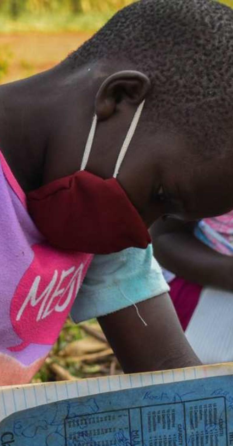 Three children writing in notebooks, outdoors, wearing facemasks