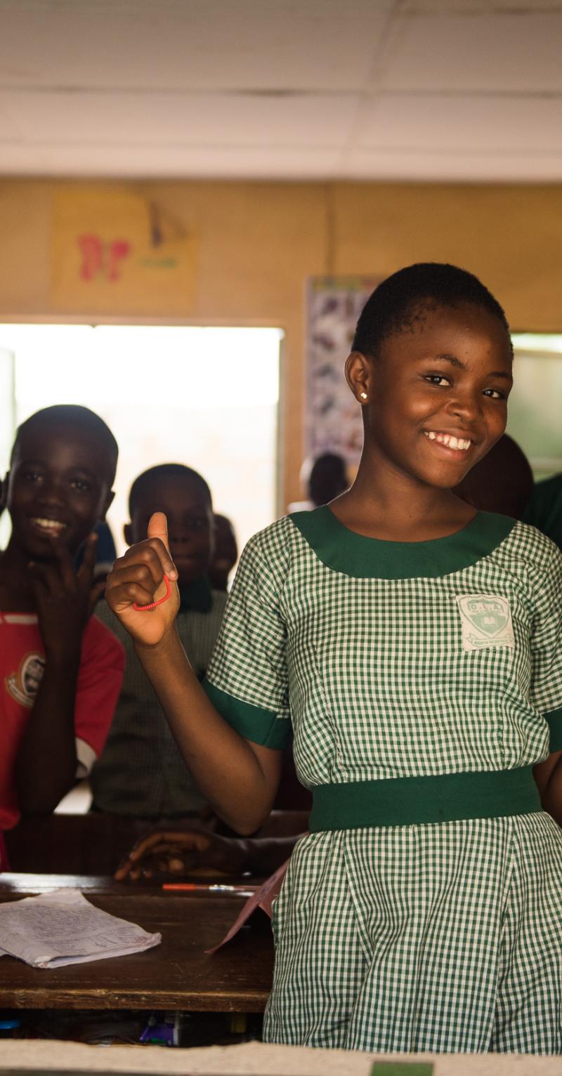 Three Black girls in green checked school uniforms smile at the camera