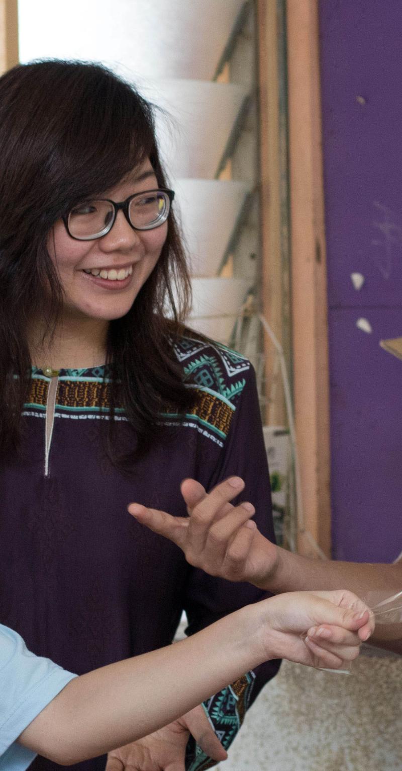 A young Asian female teacher is surrounded by 4 smiling teenage Asian students, 3 girls and a boys