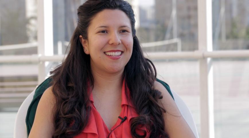 A closeup of a smiling young woman with long brown hair in a dark pink shirt