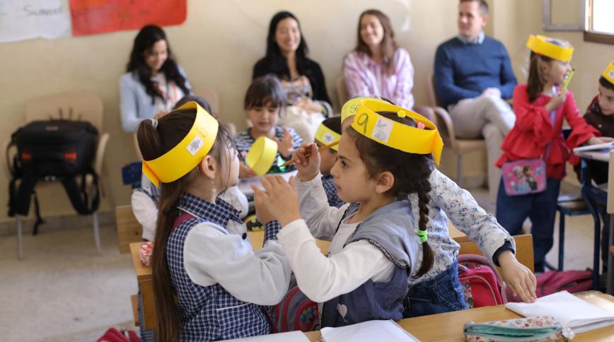 Two young girls in a classroom wearing yellow paper headbands face each other