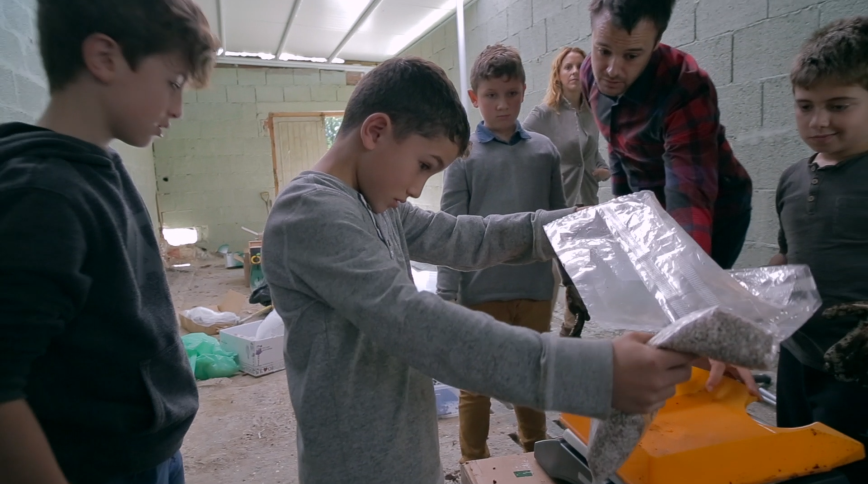 A boy holds a plastic sheet while two other boys and a young male teachers watch