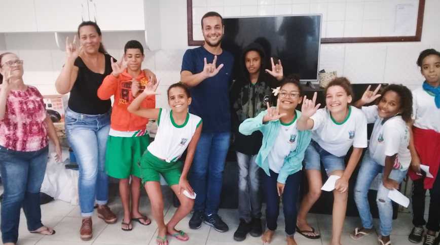 A young male teacher and a group of young teenagers smile and show peace signs