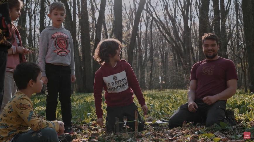 Three children and a young man with a beard are out in the woods smiling