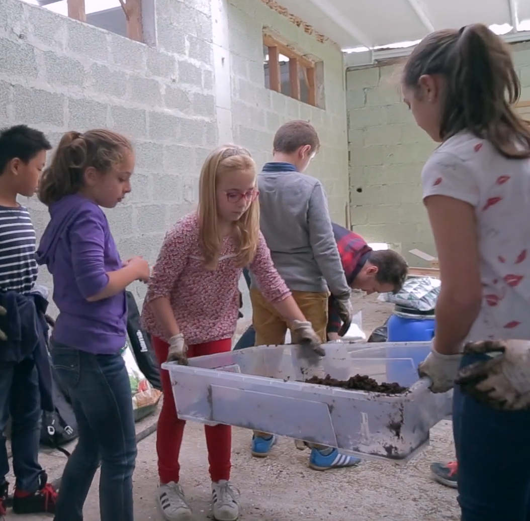 Three young girls lift a plastic bin filled with what looks like soil