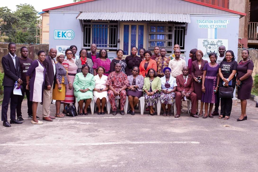 A large group of Nigerian adults poses formally for a photo where most are standing with a row of women seated in front