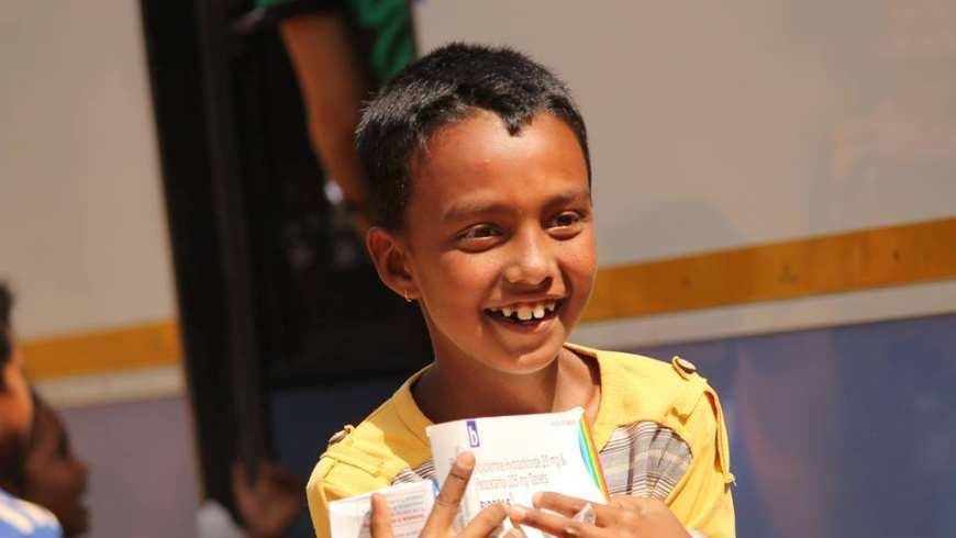 Close up of a young South Asian child holding relief supplies and smiling