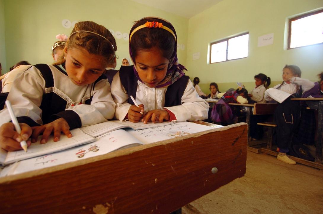 Two young girls write in workbooks at a shared desk in a classroom in Iraq
