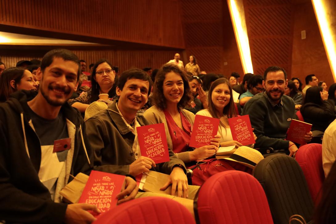 People sit in an auditorium holding up programs for Enseña Chile's 15th anniversary event