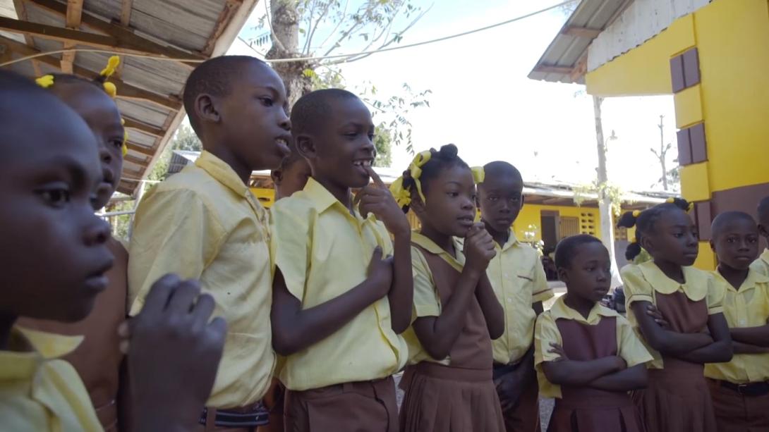Haitian students in their yellow and brown school uniforms gather in a school courtyard