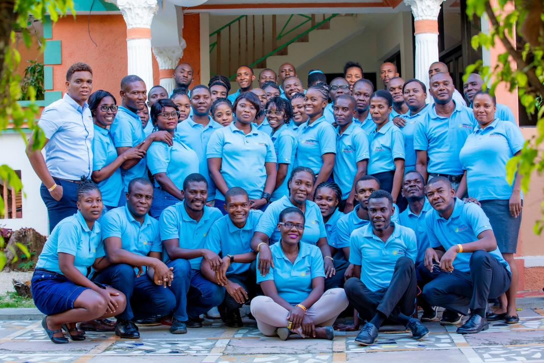 A group photo of Anseye Pou Ayiti staff in matching blue shirts posing outside their office
