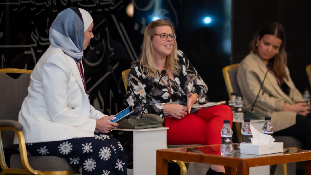 Three women sit on stage for a panel with microphones in front of them