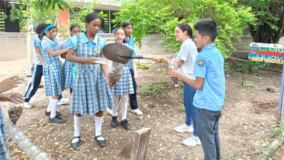 Students in school uniform stand outside holding shovels and bottles as they participate in a science experiment