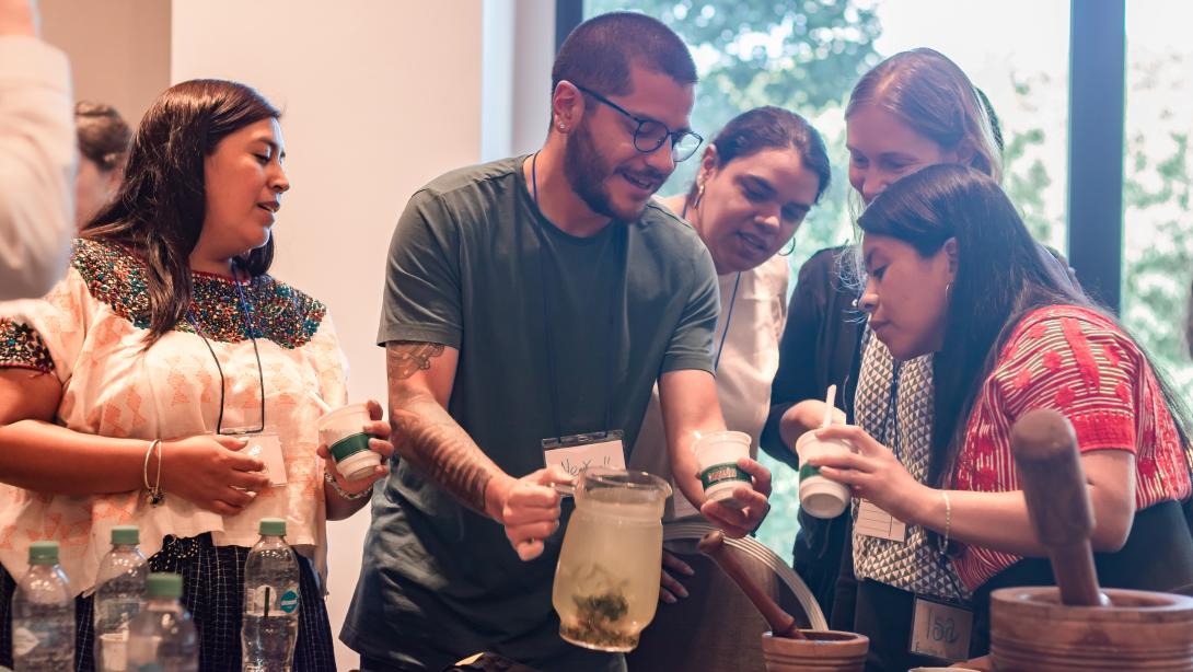 Adults stand around a table mixing a drink in a jug and mortar and pestle