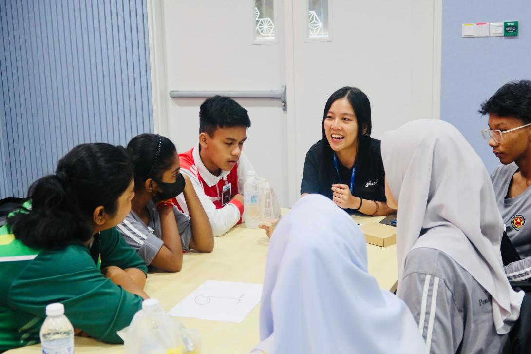 Malaysian students and a woman in a Micron polo shirt have a lively discussion around a table