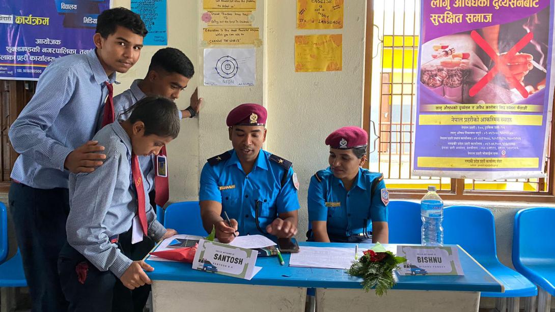 Three boys stand at a table where a male and female police officer are sitting, they are all talking to each other