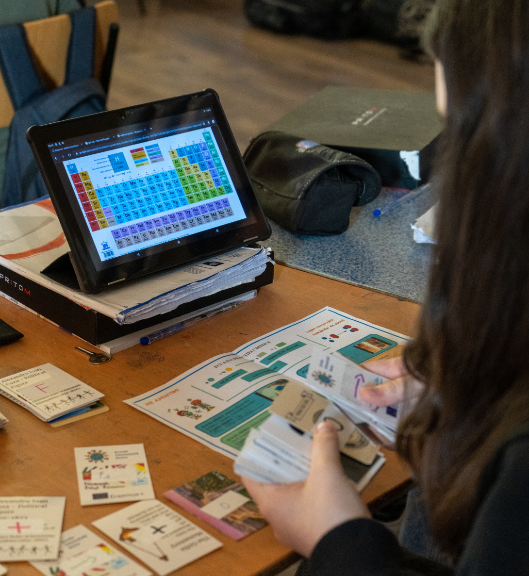 A girl sorts cards as she looks at a small computer screen with colored blocks on it 
