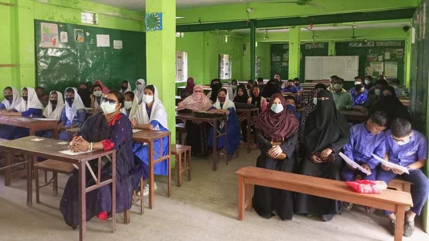 Numerous parents sit at desks in a classroom in Bangladesh
